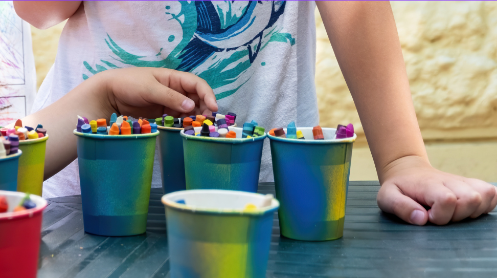 There are 4 cups, each filled with crayons. Two students are standing near the cups.